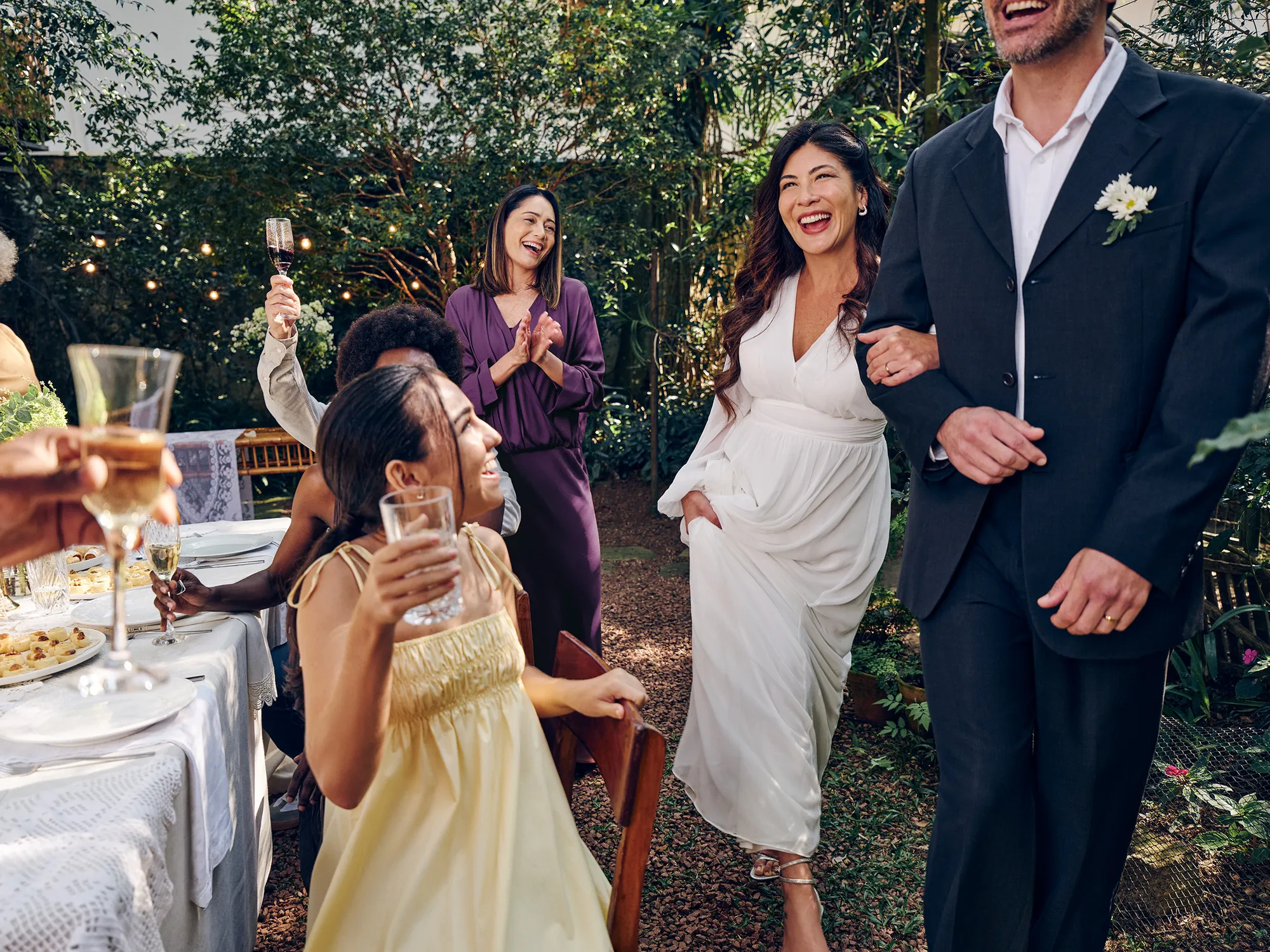 Casal de noivos em seu casamento celebrando junto com seus convidados. Na imagem, podemos ver elementos que remetem a uma festa de casamento, como os trajes sociais, copos levantados para brindar, etc.