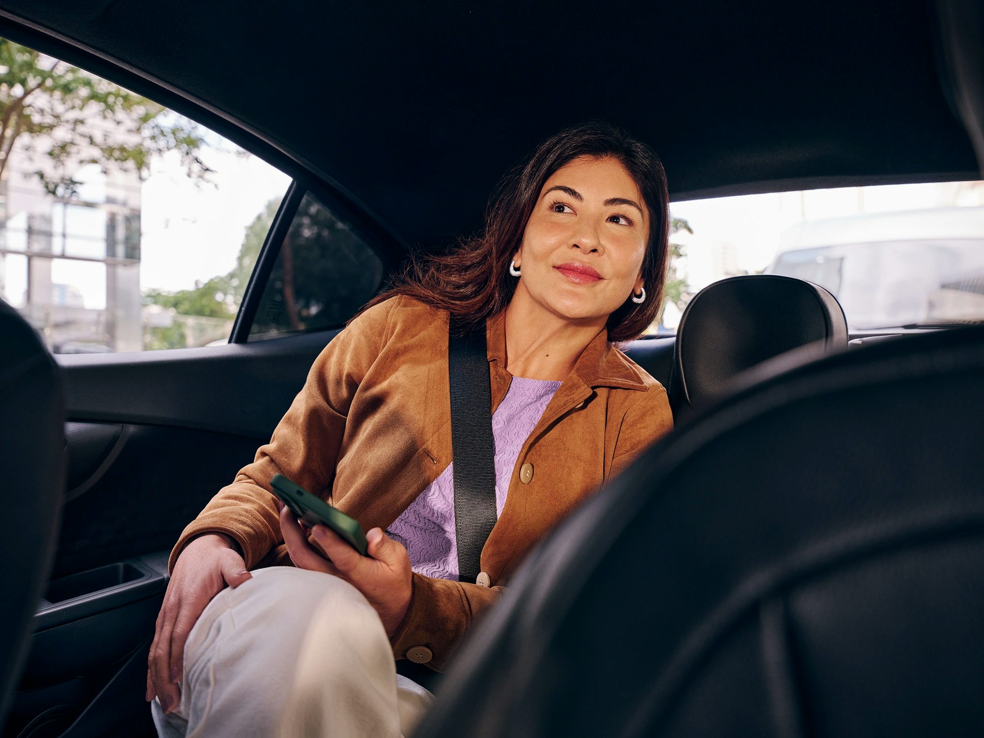 Mulher sentada no banco de trás de um carro segurando um celular em suas mãos