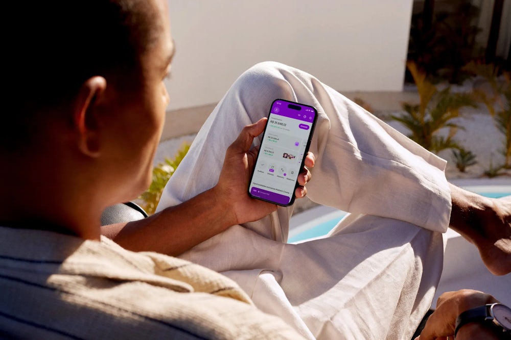 Homem sentado olhando para o celular com o aplicativo do Nubank aberto