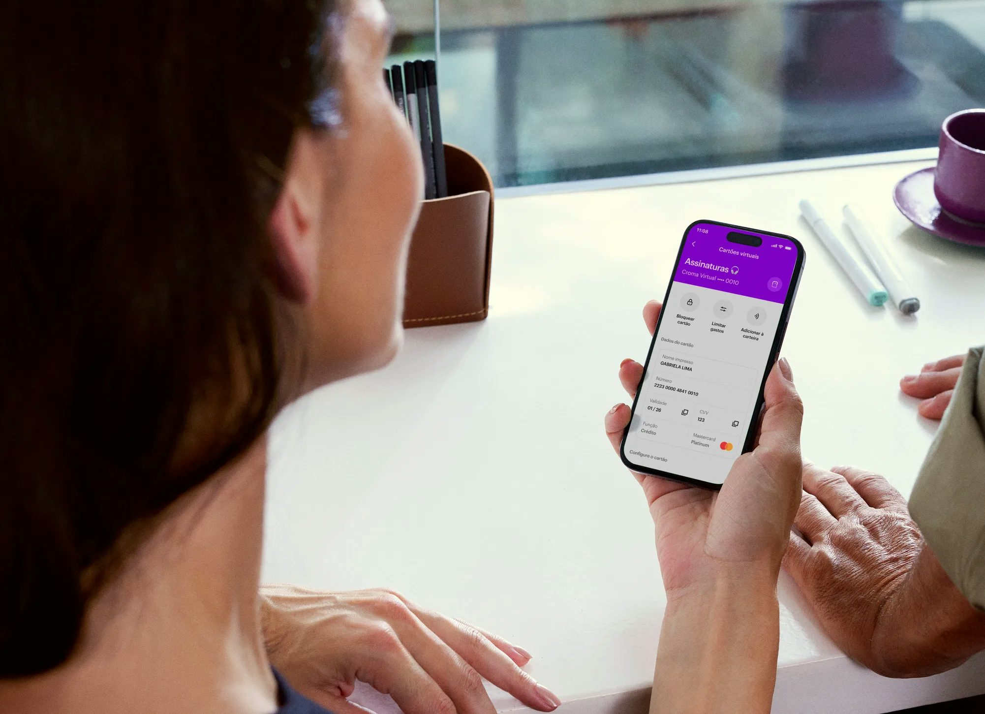 Mulher segurando o celular com o aplicativo do Nubank aberto. No celular, podemos ver que ela está acessando a sessão de Assinaturas de Nubank Croma