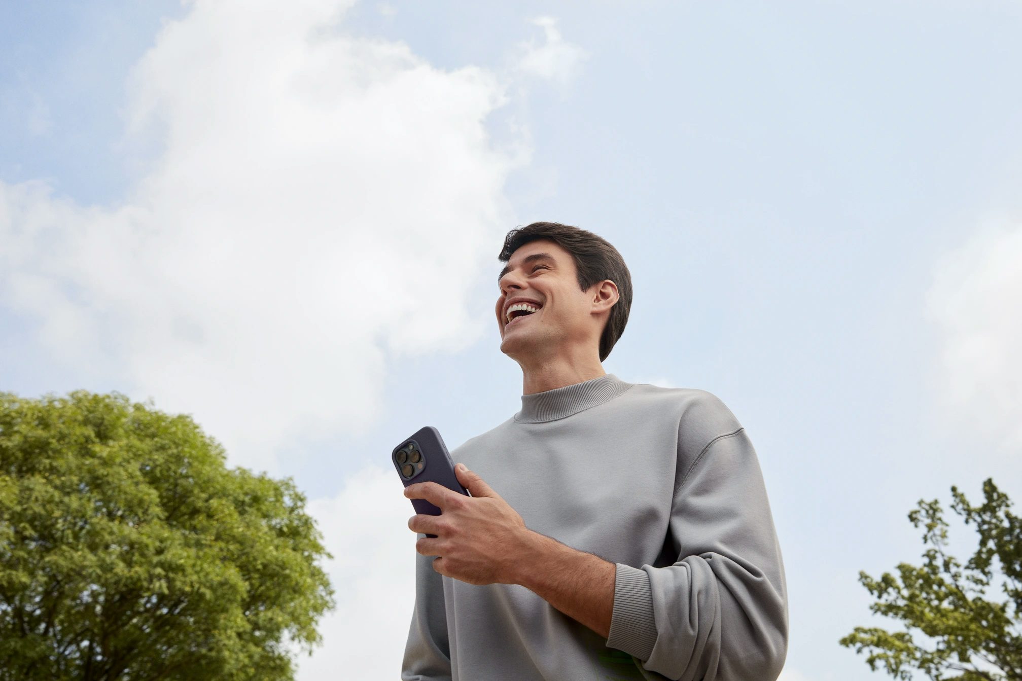 Homem sorrindo ao ar livre com celular na mão