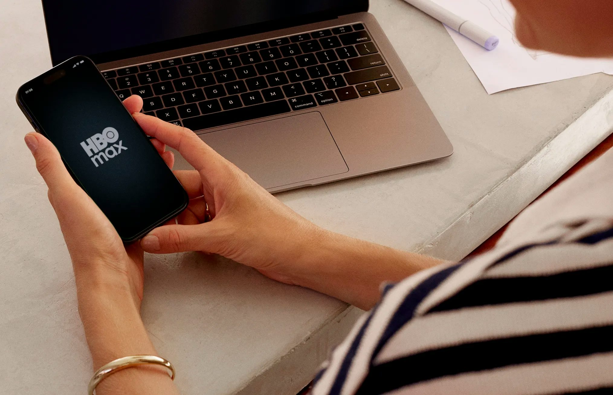 Mulher segurando o celular com o aplicativo do Nubank aberto. No celular, podemos ver que ela está ativando HBO Max com desconto, um benefício Nubank Croma