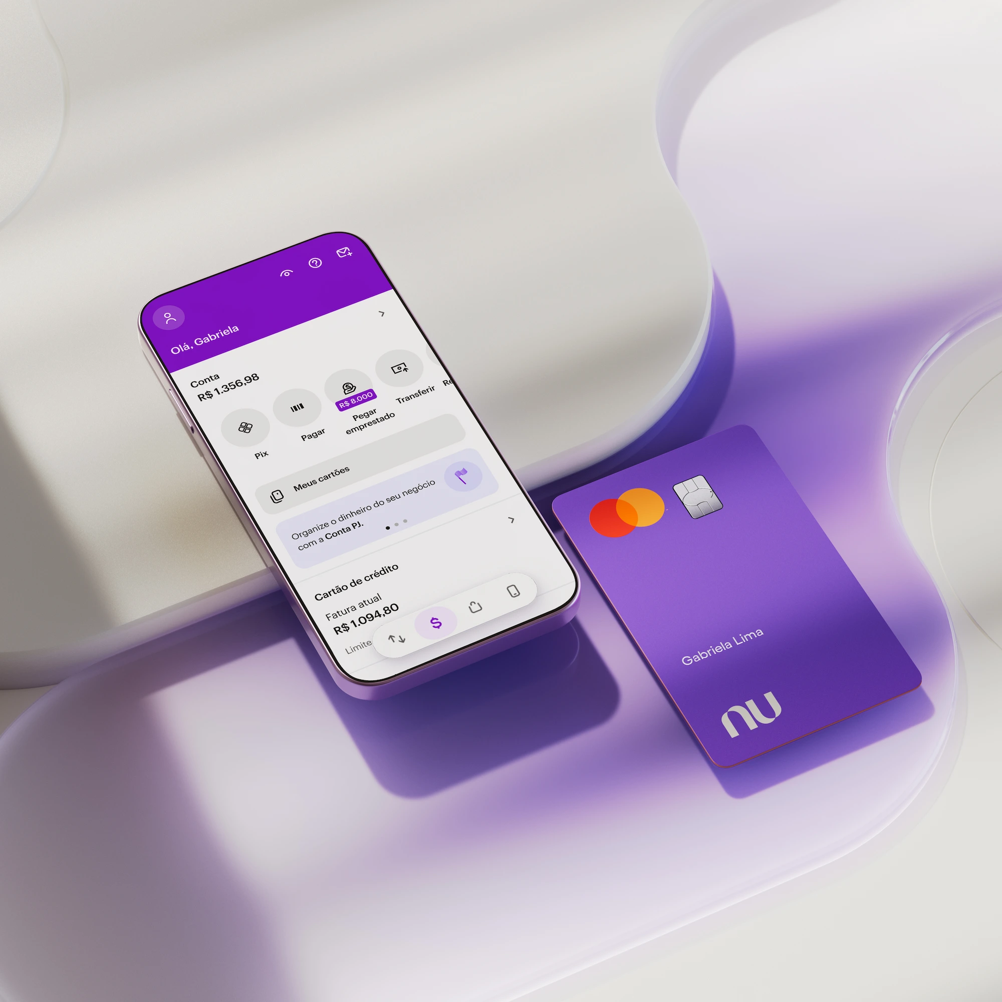 Celular com aplicativo Nubank aberto na área inicial com o saldo da conta na parte superior da tela. Na parte inferior do aplicativo na tela do celular, informações sobre Cartão de crédito. O celular e o cartão estão deitados apoiados em uma forma geométrica branca.