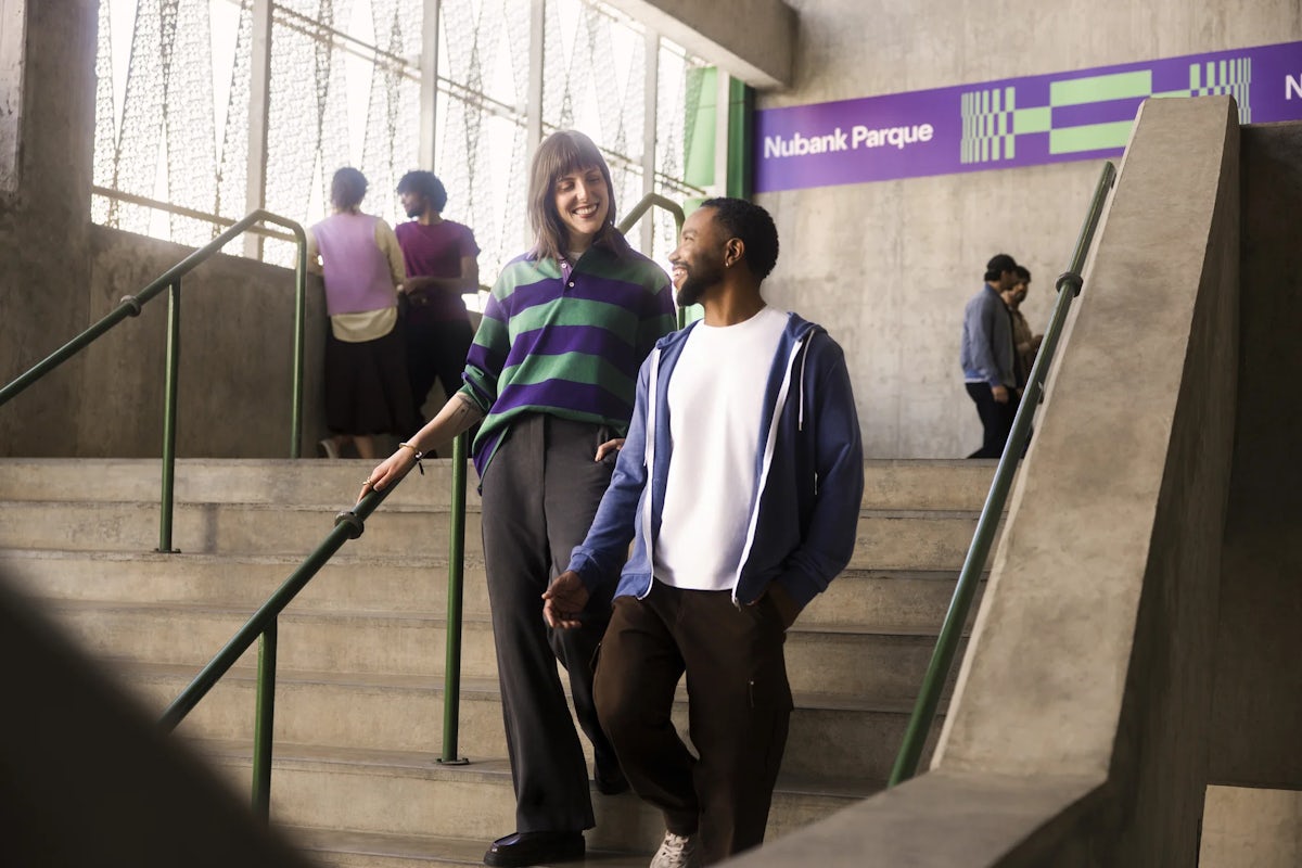 Um homem e uma mulher conversando na escada do eatádio, com uma faixa de Nubank Parque atrás