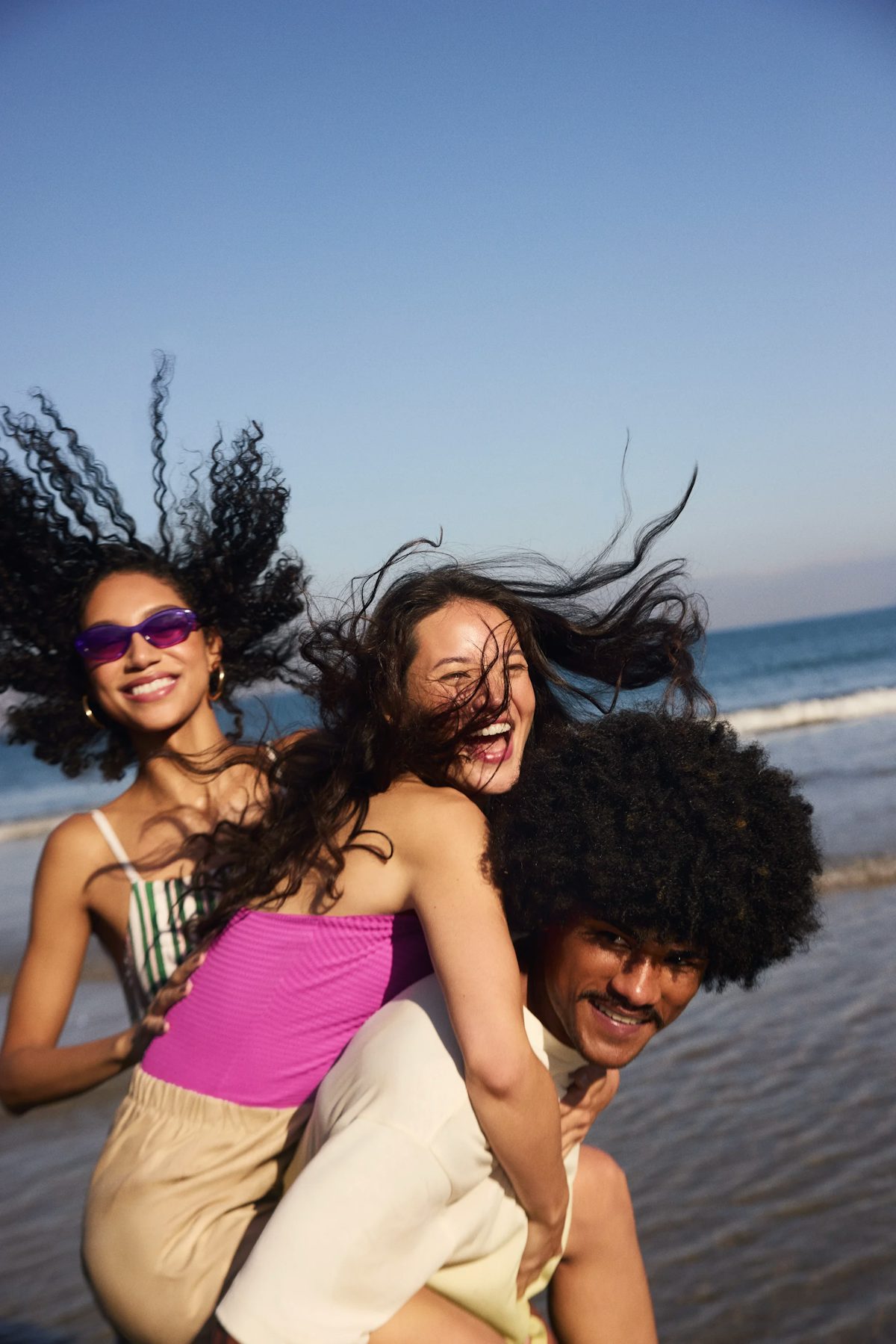 Três amigos se divertindo na praia com cabelos ao vento.