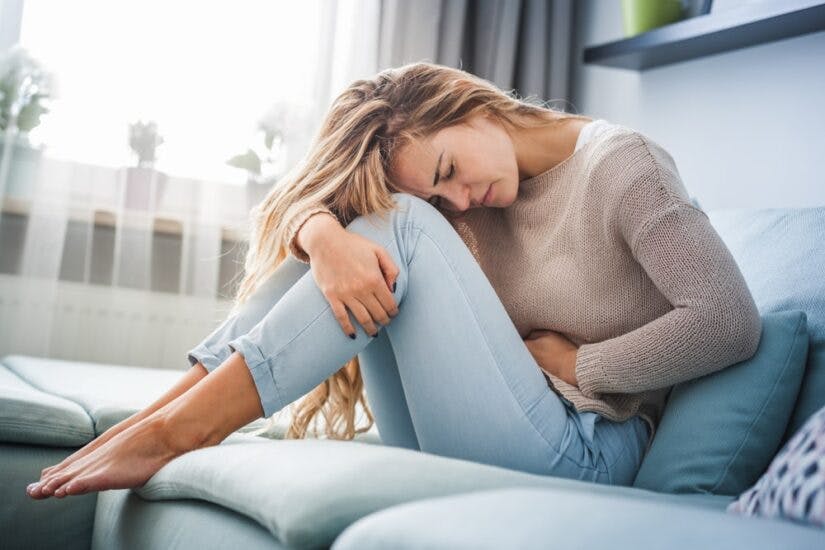 A Woman Sitting On The Couch Holding Her Stomach In Pain