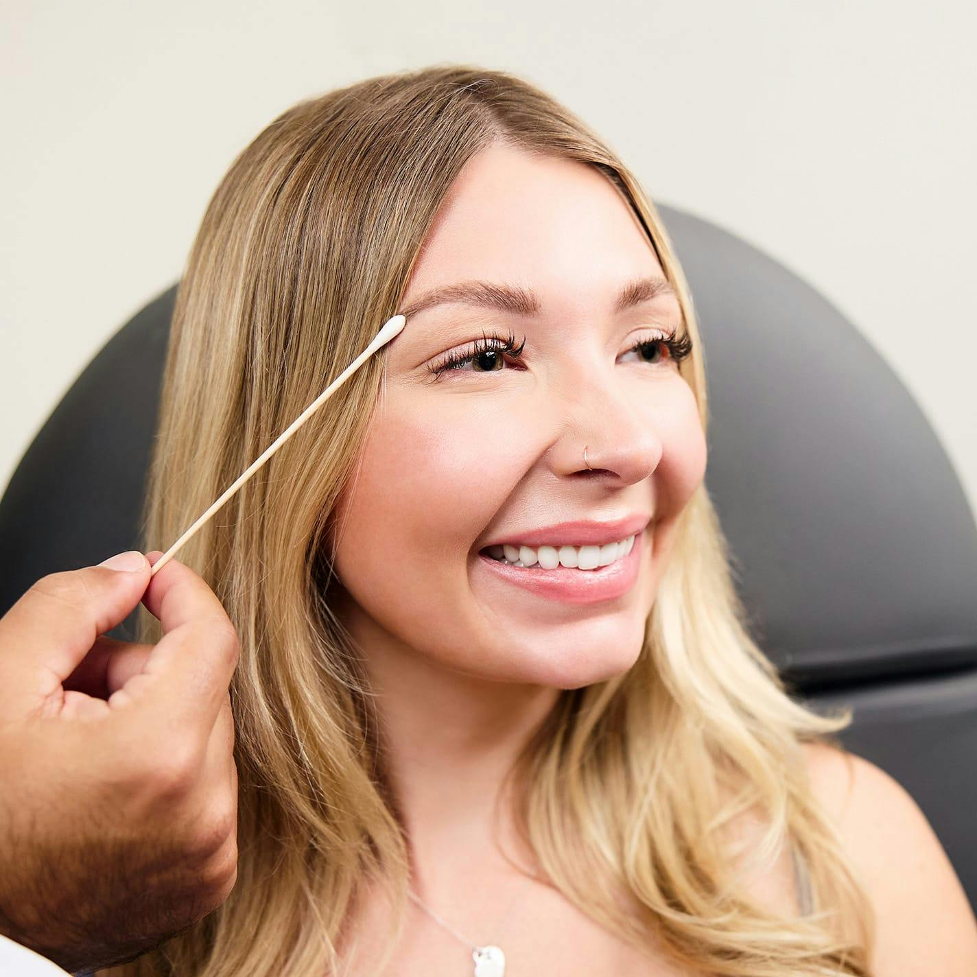 woman with blonde hair with q-tip to her eyebrow