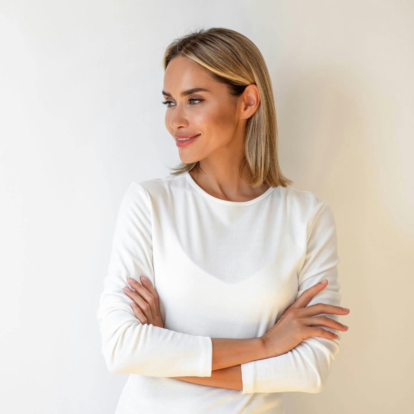woman with short blonde hair in white dress crossing her arms looking to the left