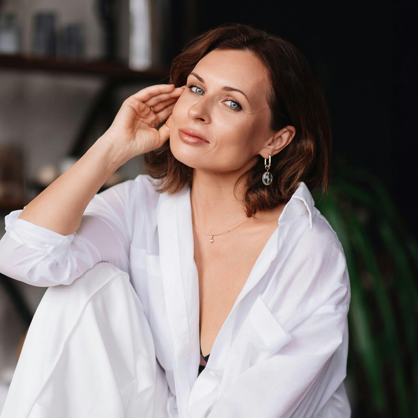 woman with short brown hair in all white outfit with hand near her ear