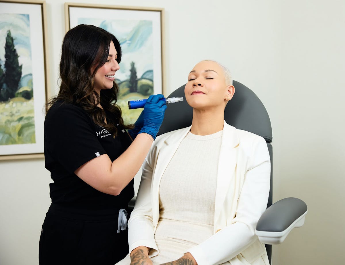 patient sitting eyes closed while nurse holds microneedling machine to her cheek
