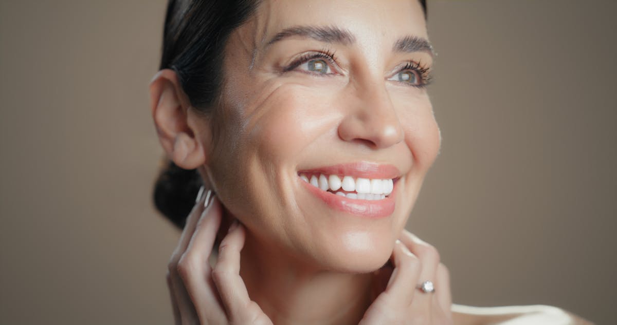 Older woman with brown hair smiles looking off in a studio shoot. Her definited jaw line, and tight skin emulates the potential results of a Nashville Facelift with Dr. Higdon