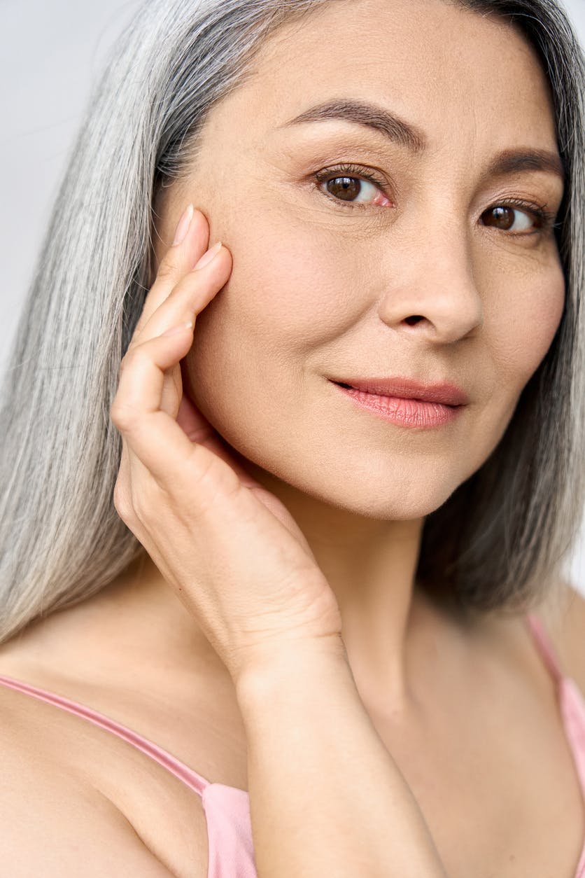 Beautiful older woman with gray hair smiles at the camera with her hand up to her face. Her bright eyes show the potential results of a blepharoplasty in Franklin and Nasvhille with Dr. Higdon