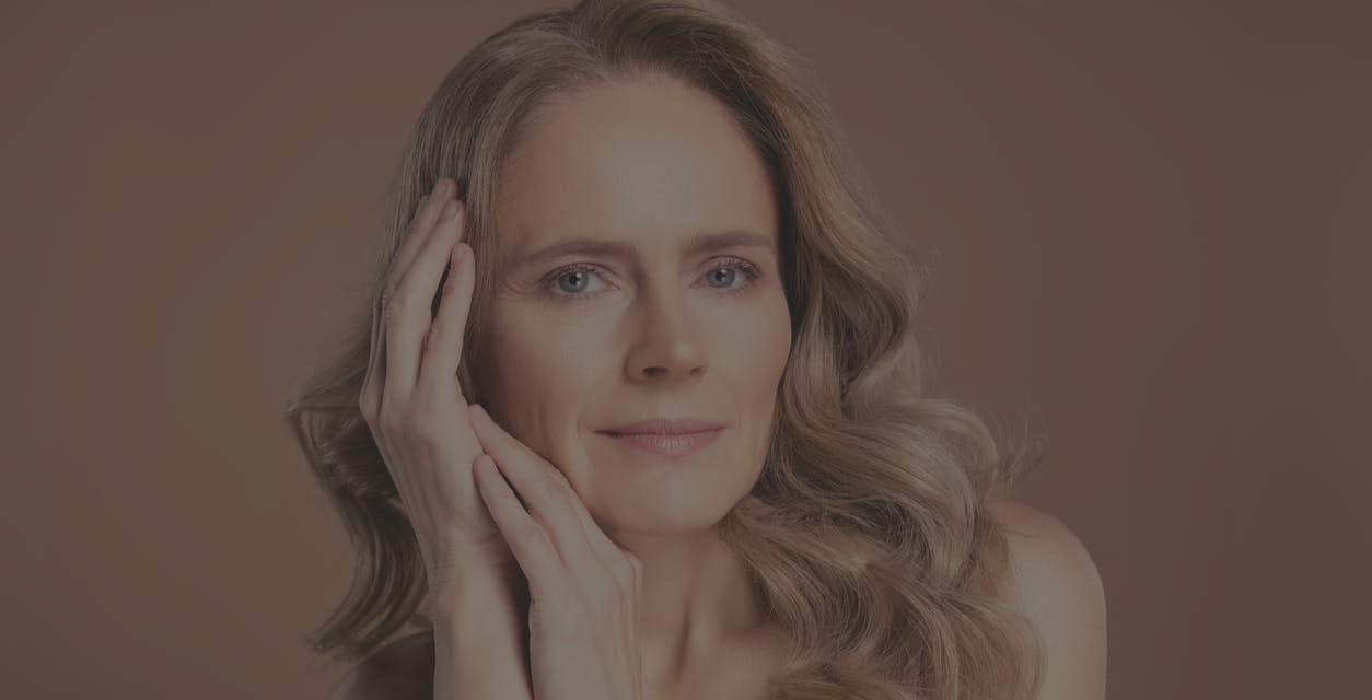 Beautiful older woman with long hair smiles at the camera with her hands up to her face. Her bright eyes show the potential results of a blepharoplasty in Franklin and Nasvhille with Dr. Higdon