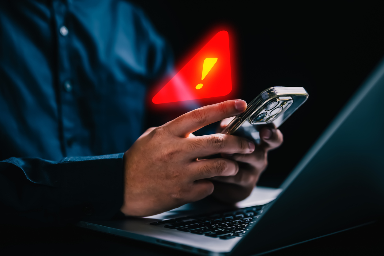 Man holding a phone near his laptop with a warning sign