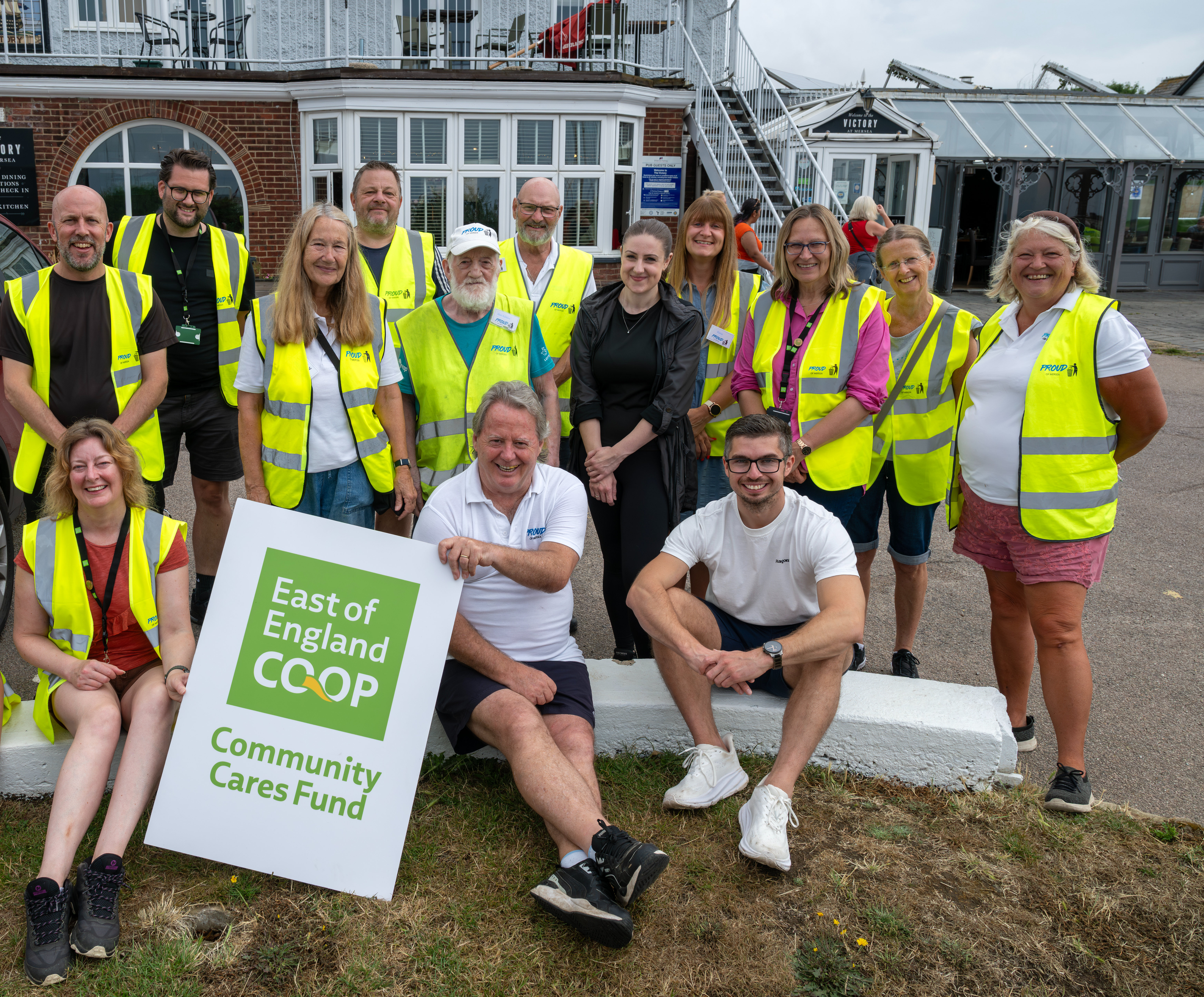 Group of volunteers in yellow hi-vis jackets holding an East of England Co-op Community Cares Fund sign during a community litter pick