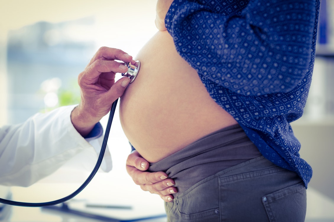 Arzt hört Herztöne des ungeborenen Babys am Bauch der werdenden Mutter ab