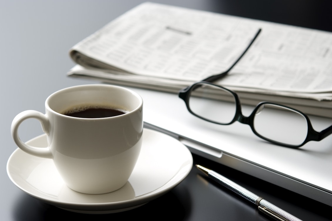 Arbeitsplatz mit Kaffeetasse, Laptop , Brille und Zeitung