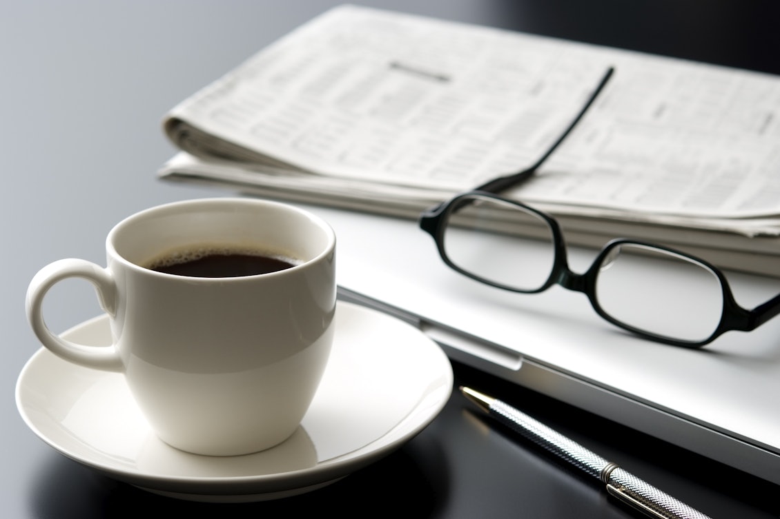 Arbeitsplatz mit Kaffeetasse, Laptop , Brille und Zeitung Arbeitsplatz mit Kaffeetasse, Laptop , Brille und Zeitung