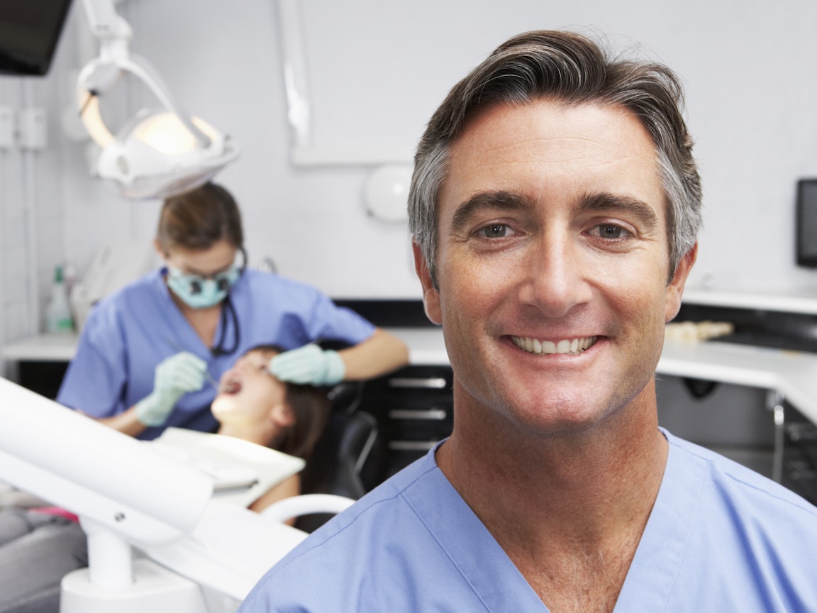 Zahnarzt steht im Vordergrund, Zahnärztin behandelt Patienten