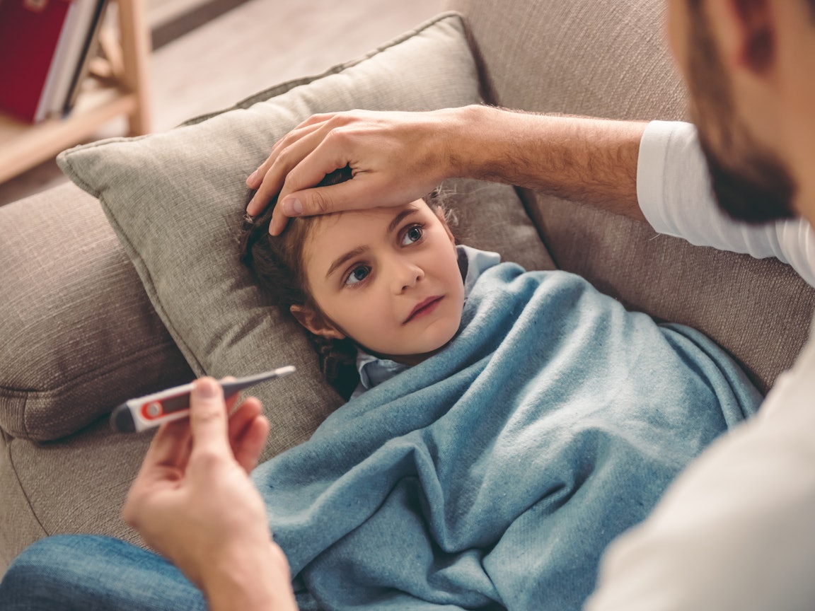 Krankes Mädchen liegt auf dem Sofa und bekommt Fieber gemessen