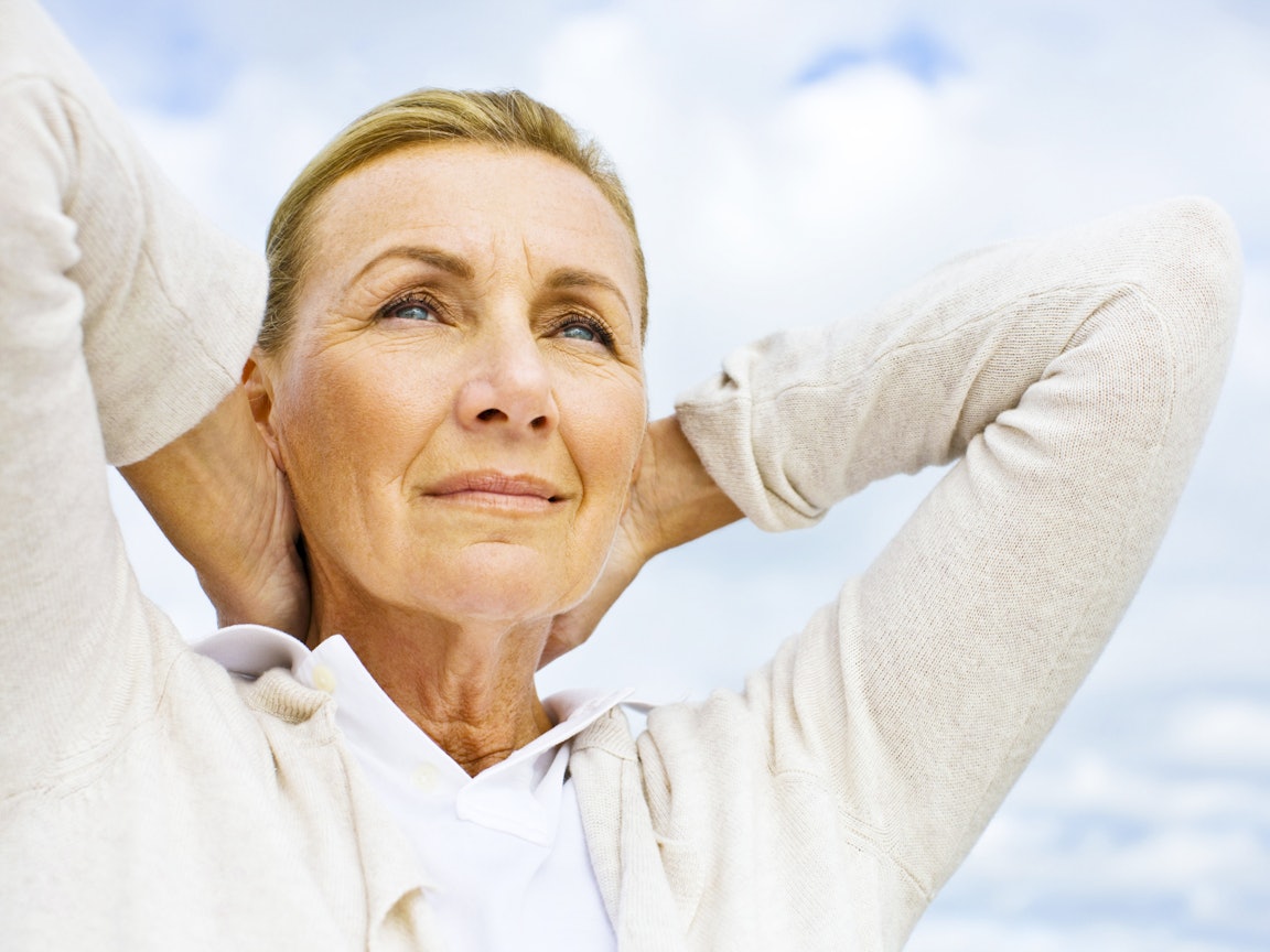 Ältere Frau steht draussen und verschränkt die Arme hinter dem Kopf Ältere Frau steht draussen und verschränkt die Arme hinter dem Kopf