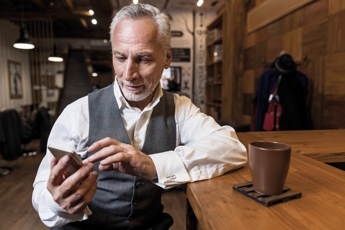 Älterer Mann sitzt an der Theke und schaut in ein Smartphone