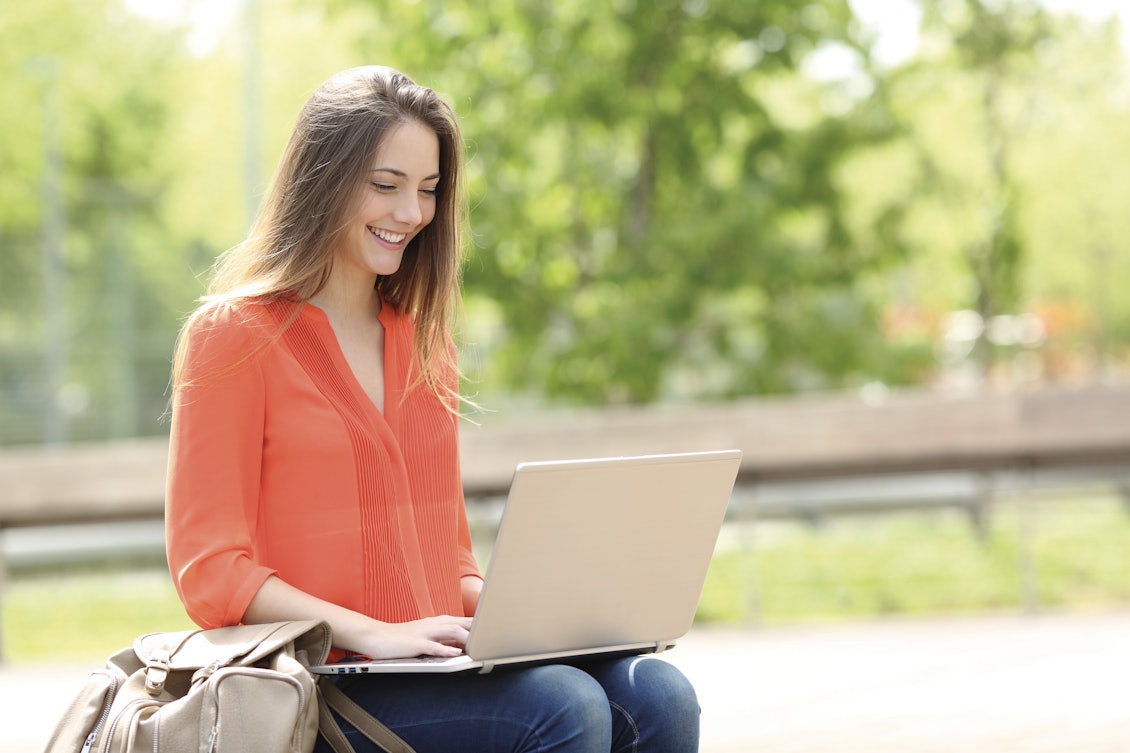 Junge Frau sitzt mit einem Laptop im Park und arbeitet (vielleicht)