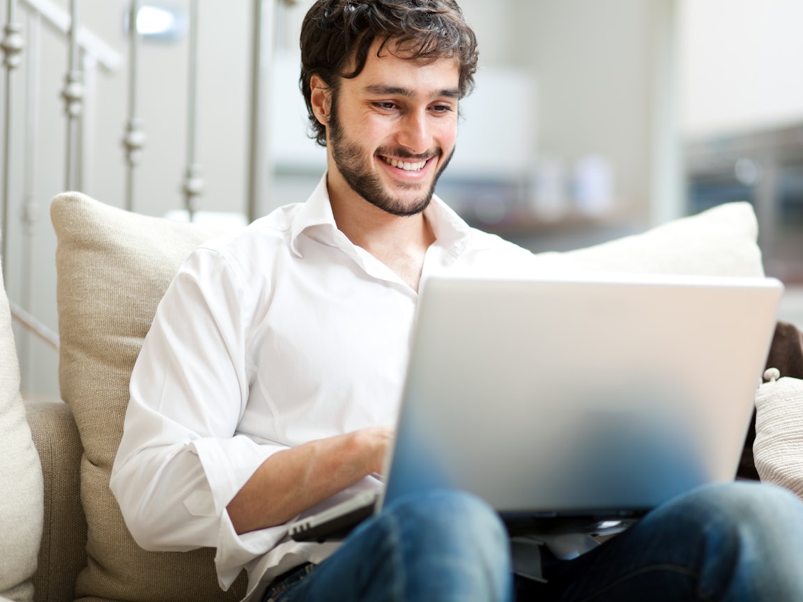 Junger Mann sitzt am Laptop und freut sich Junger Mann sitzt am Laptop und freut sich