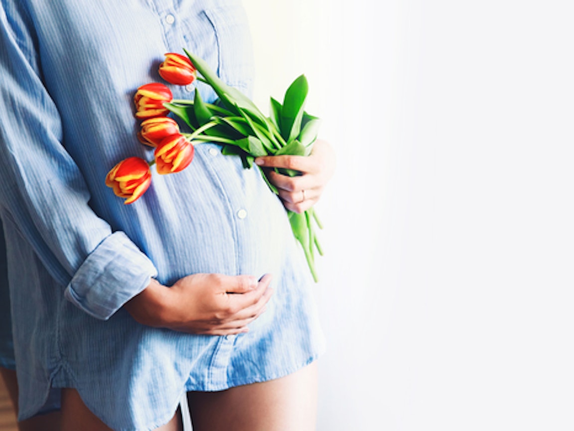 Frau mit Babybauch hält Tulpen in der Hand