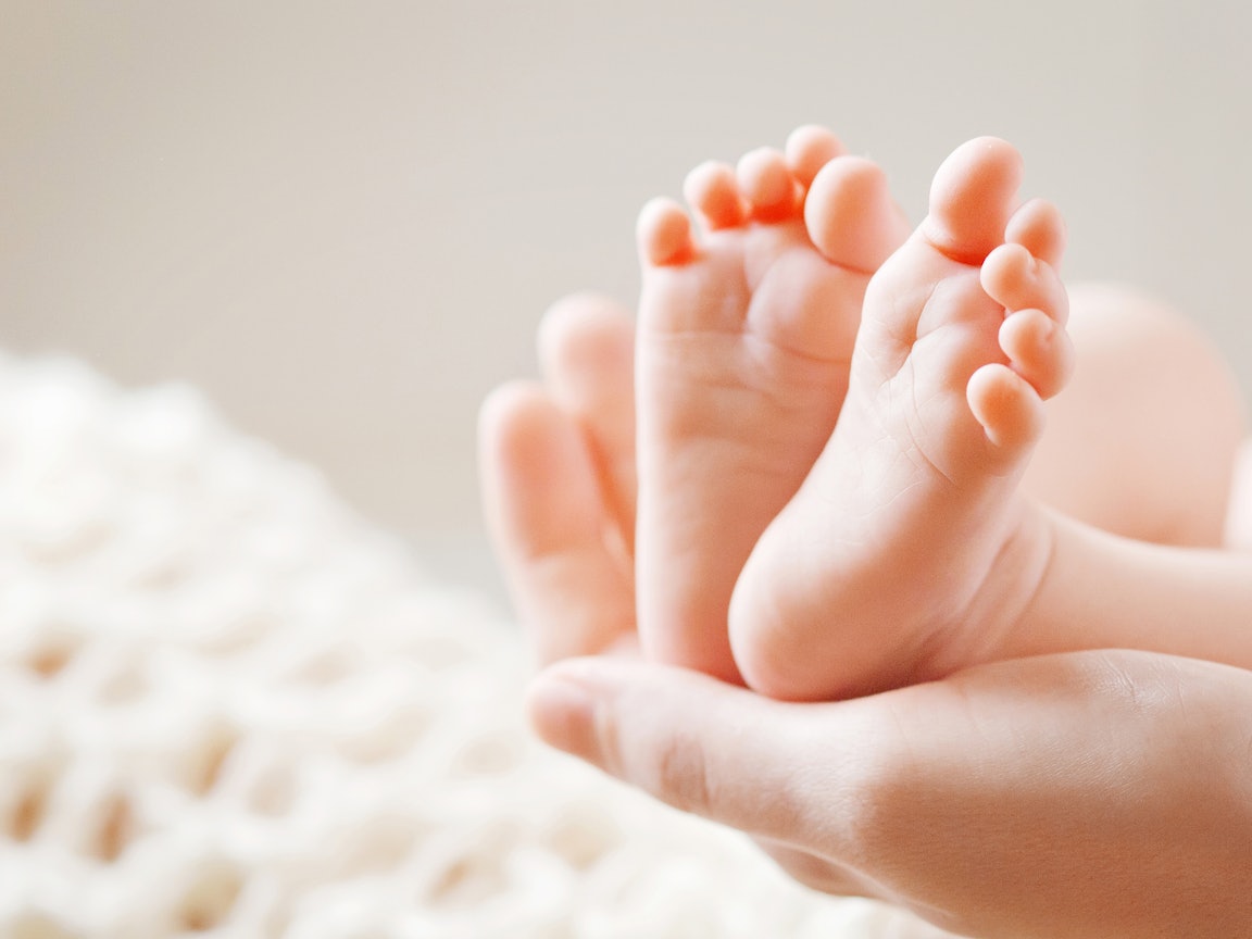 Hand umfasst die Füße eines Babies