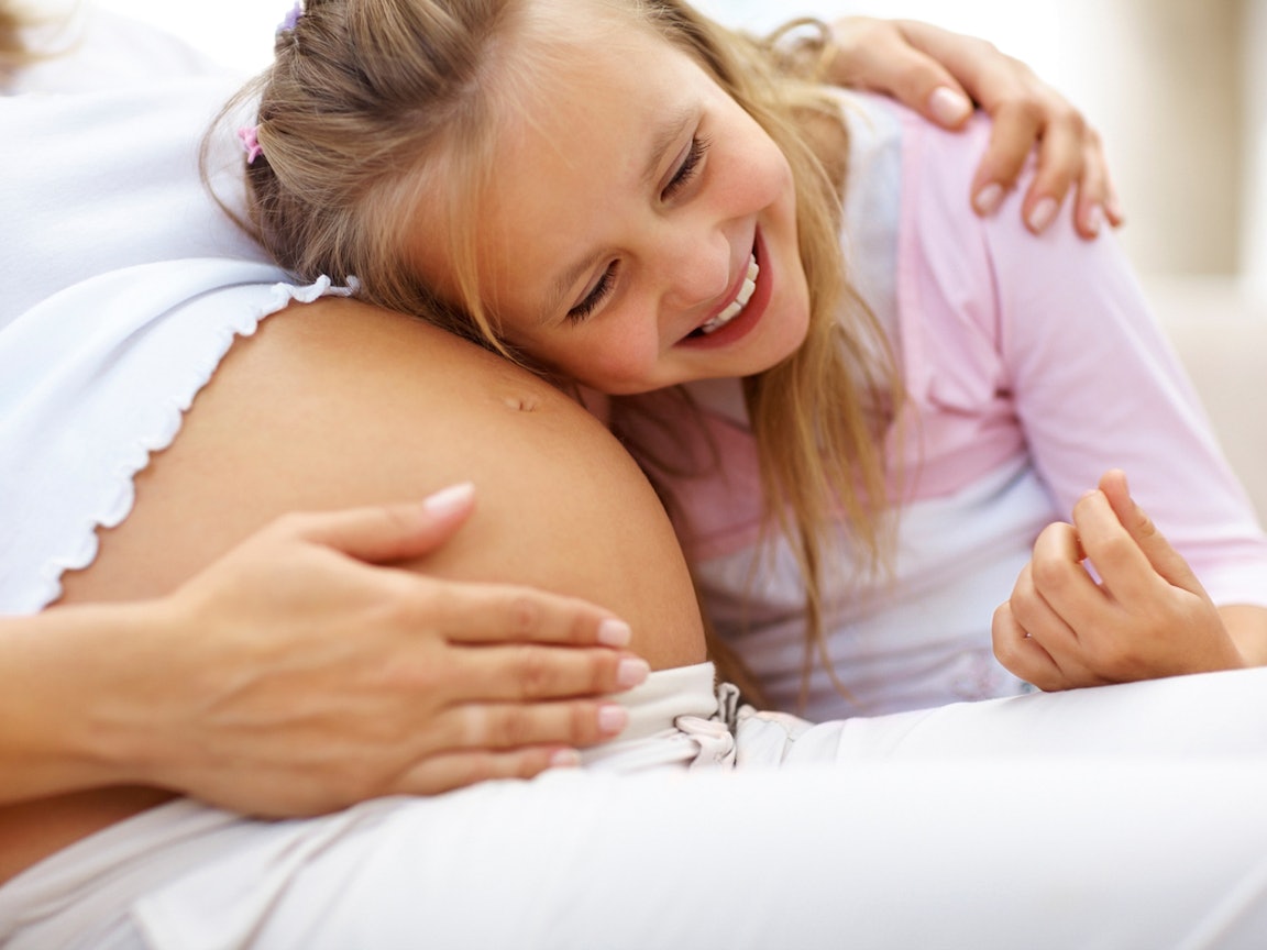 Mädchen hört am Babybauch ihrer Mutter Mädchen hört am Babybauch ihrer Mutter