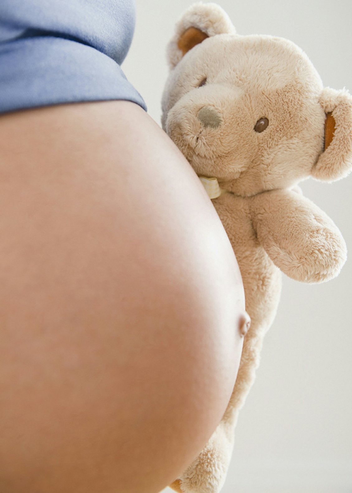 Babybauch im Vordergrund mit Teddy im Hintergrund Babybauch im Vordergrund mit Teddy im Hintergrund