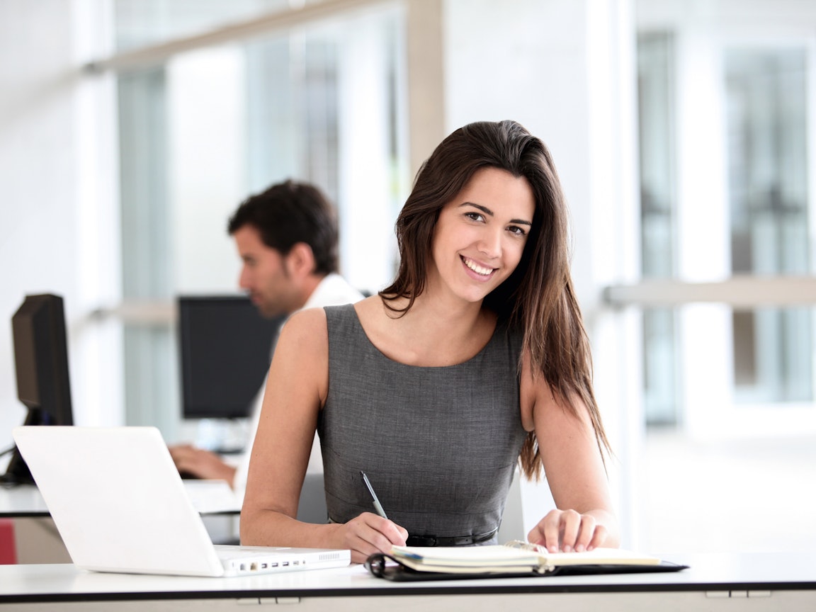 Junge Frau sitzt mit einem Ordner im Büro am PC Junge Frau sitzt mit einem Ordner im Büro am PC