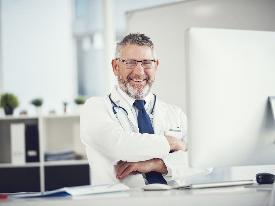 Arzt sitzt lächelnd am Schreibtisch Arzt sitzt lächelnd am Schreibtisch