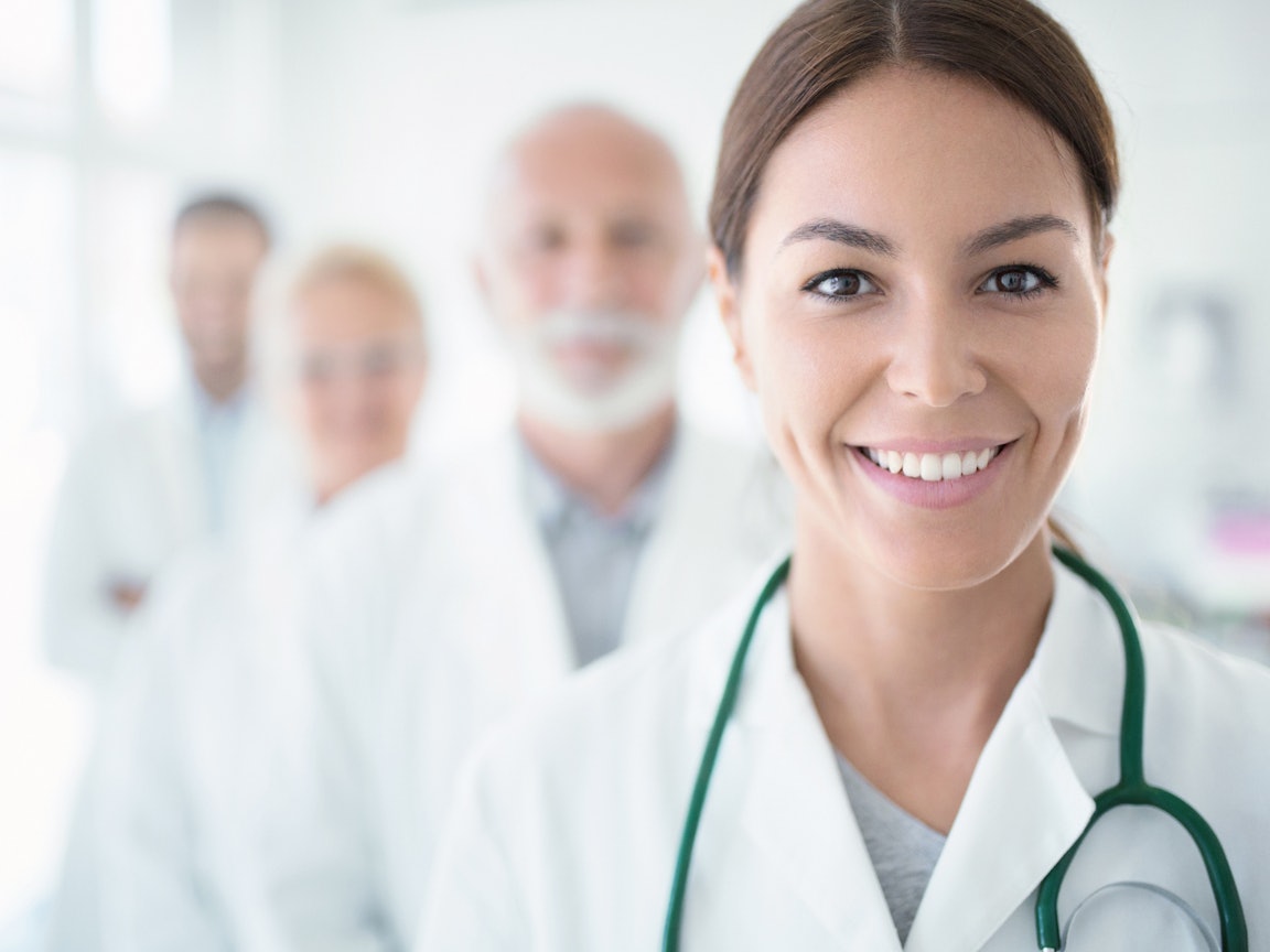 Junge Ärztin steht vor einer Gruppe Ärzte Junge Ärztin steht vor einer Gruppe Ärzte