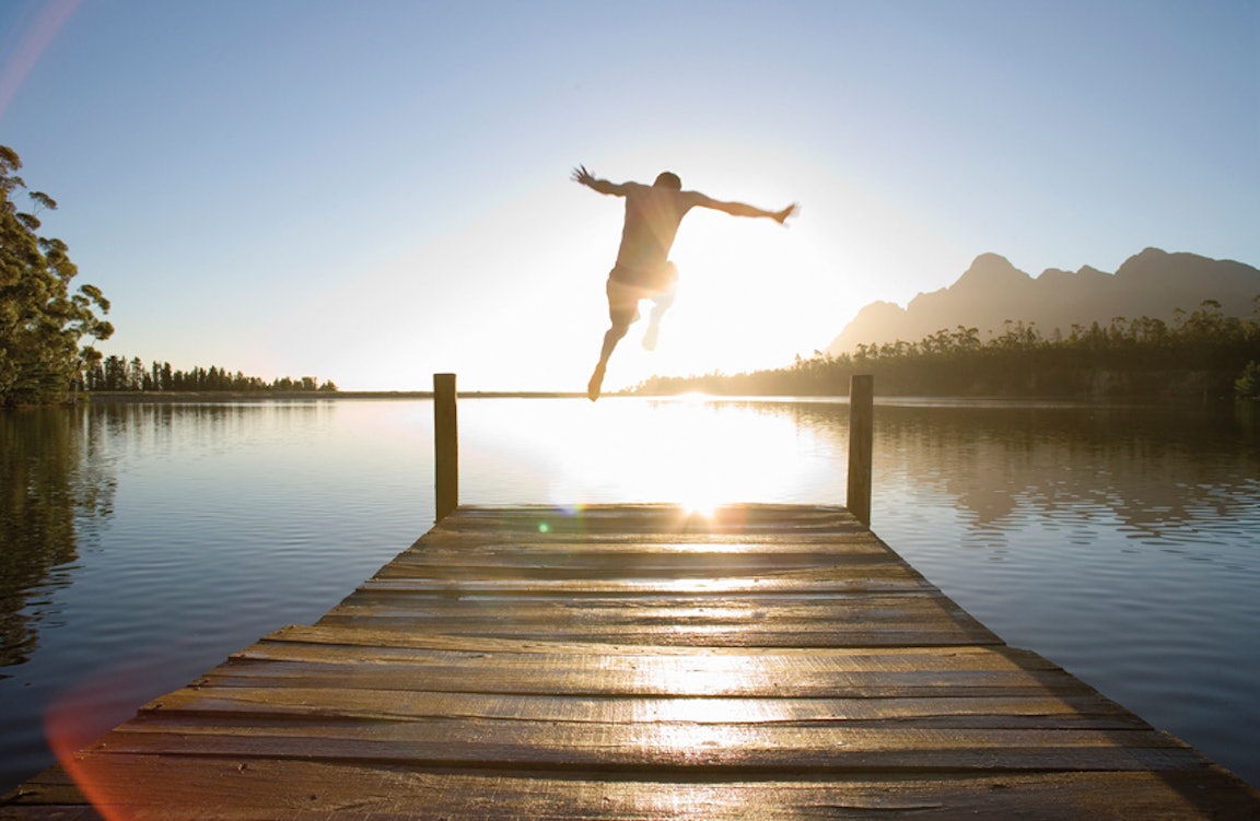 Mann springt bei Sonnenaufgang vom Steg in einen See