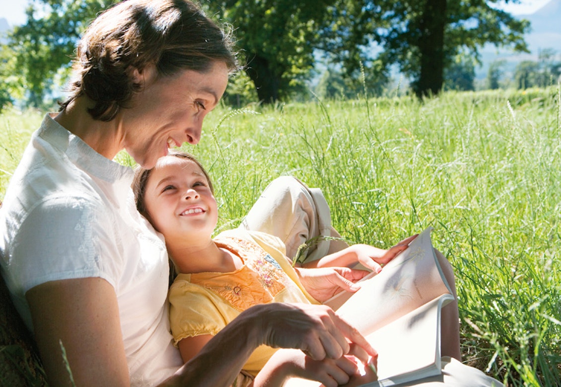 Mutter und Tochter lesen ein Buch auf einer grünen Wiese bei Sonnenschein