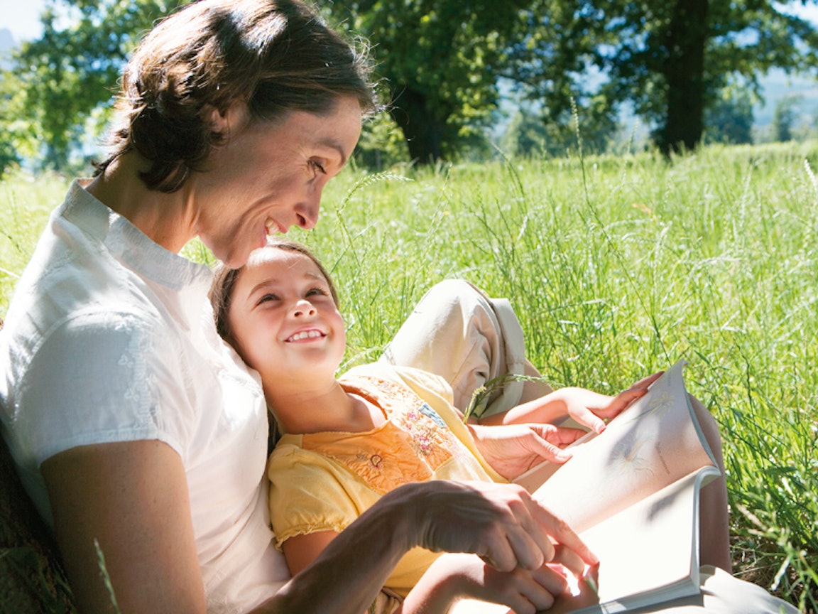 Mutter und Tochter lesen ein Buch auf einer grünen Wiese bei Sonnenschein