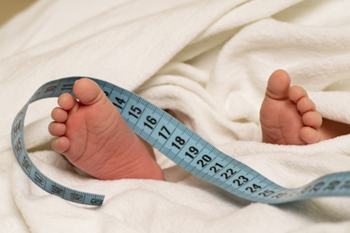 Babyfüße mit einem Maßband Ein Maßband liegt auf Babyfüßen