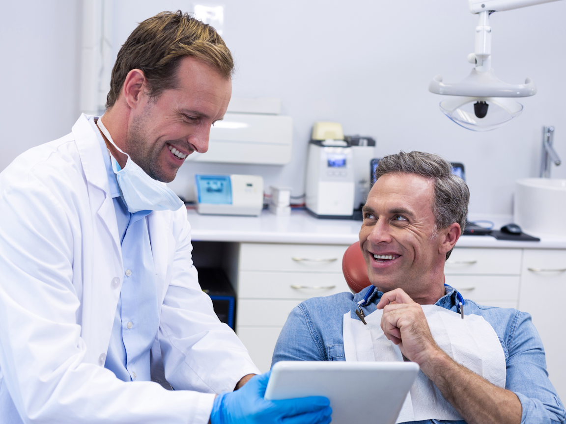 Zahnarzt berät einen Patienten mit Hilfe eines Tablets
