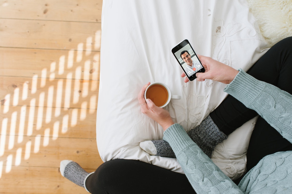 Eine Frau sitzt auf dem Bett und telefoniert mit einem TeleClinic Arzt