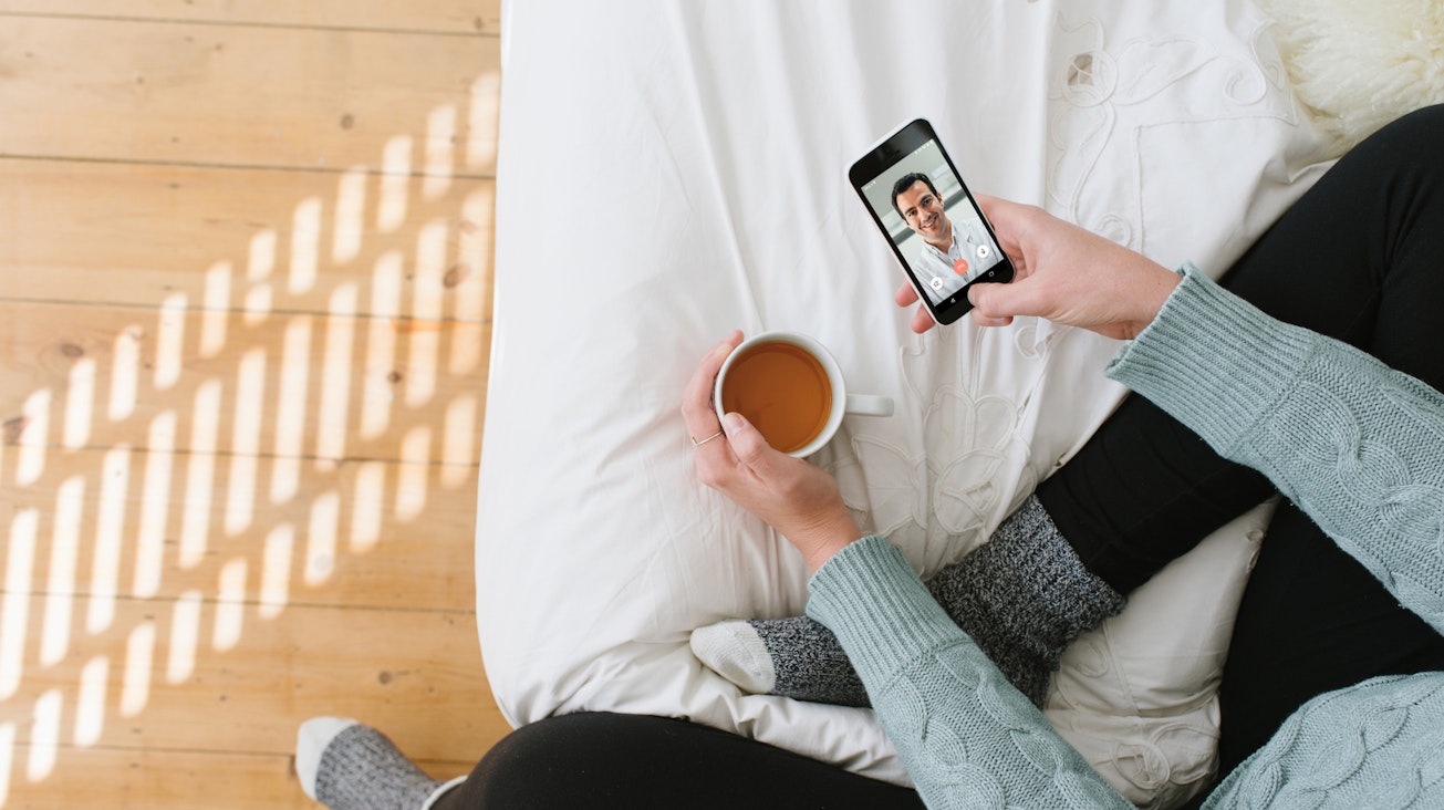 Gespräch mit einem Arzt der TeleClinic Eine Frau sitzt auf dem Bett und telefoniert mit einem TeleClinic Arzt