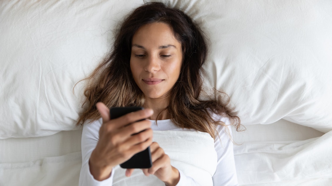 Eine Frau nutzt die TeleClinic App während sie im Bett liegt