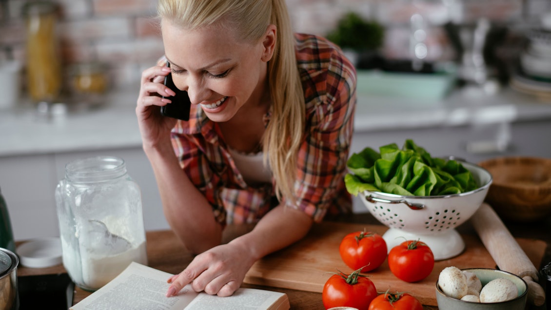 Frau beim Kochen am Handy Junge Frau in der Küche mit Buch und Handy in der Hand