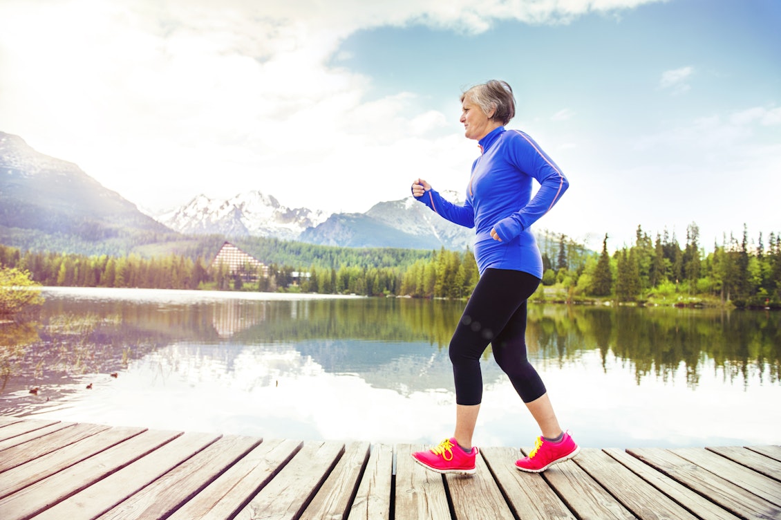 Ältere Dame beim Laufen an einem See Dame mit Sportoutift ist Joggen an einem See