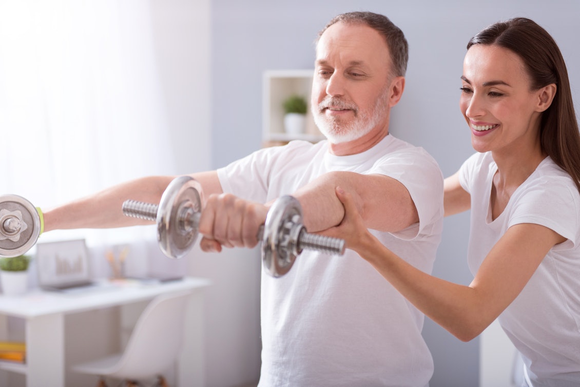 Mann bei der Physiotherapie Ein Mann stemmt unter Anleitung einer Physiotherapeutin Hanteln