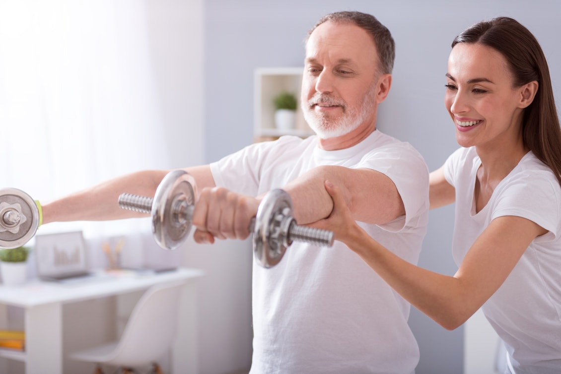 Ein Mann stemmt unter Anleitung einer Physiotherapeutin Hanteln