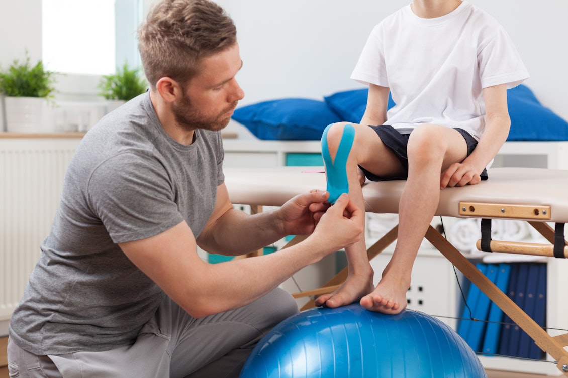 Kleiner Junge bei der Physiotherapie Ein Kind bekommt das Knie getaped