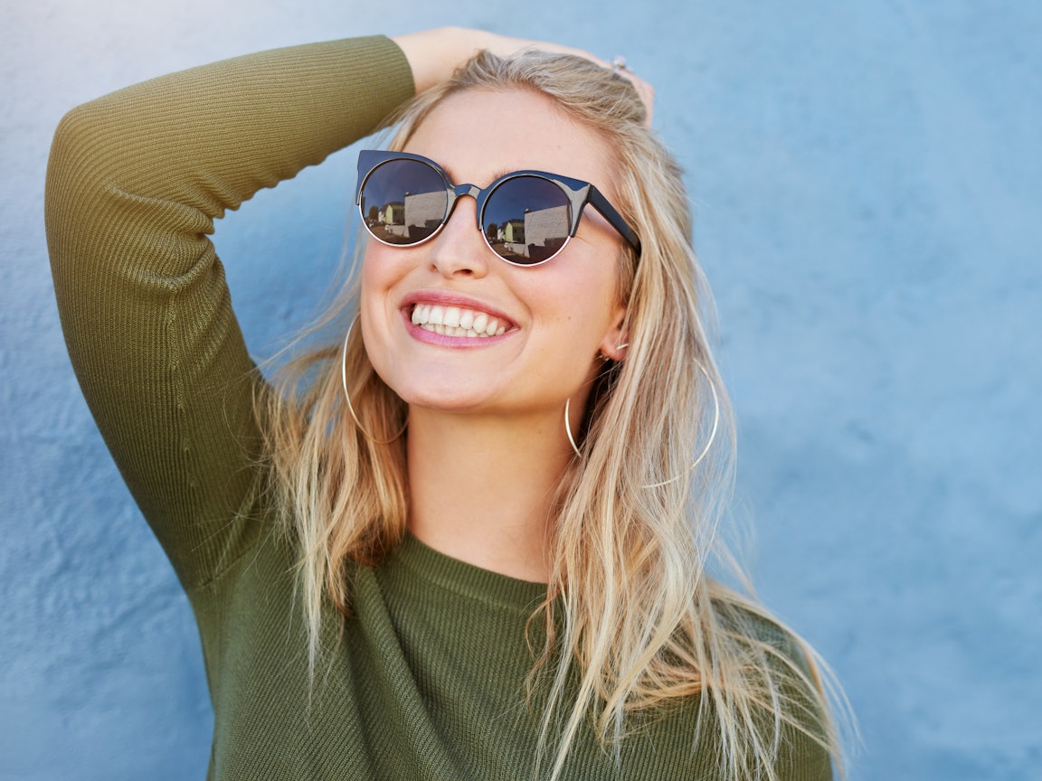 Eine junge, lächelnde, blonde Frau mit Sonnenbrille