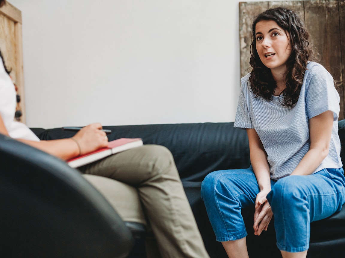 Frau im Gespräch mit Therapeutin  Eine junge Frau sitzt auf einer Couch und spricht mit der Therapeutin